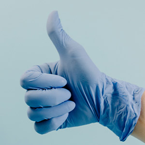 Hand mit hellblauem OP-Handschuh macht das Daumen hoch Zeichen.